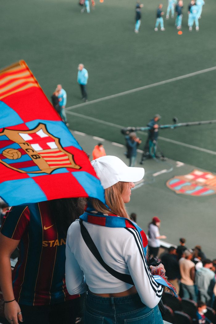 A woman in a stadium with a Barcelona football flag, watching a match.