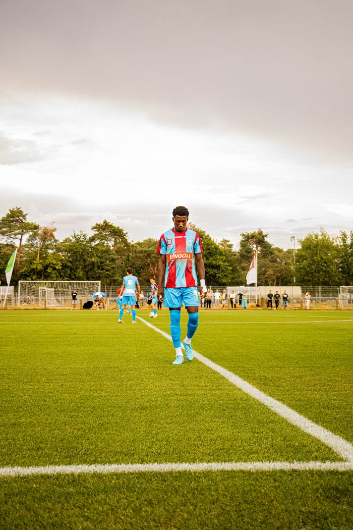 A soccer player in vibrant uniform walks on a lush green field in Lommel, Belgium.