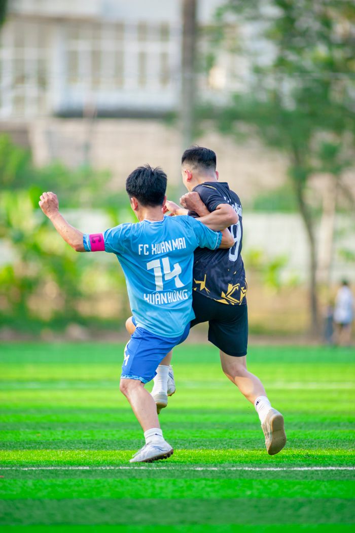 Two players vie for the ball in an exciting soccer match on a sunny day in Hanoi.