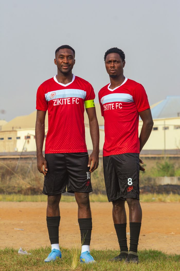 Two soccer players in red Zikite FC jerseys posing outdoors on a field.